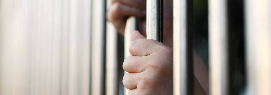 Hands behind jail cell bars