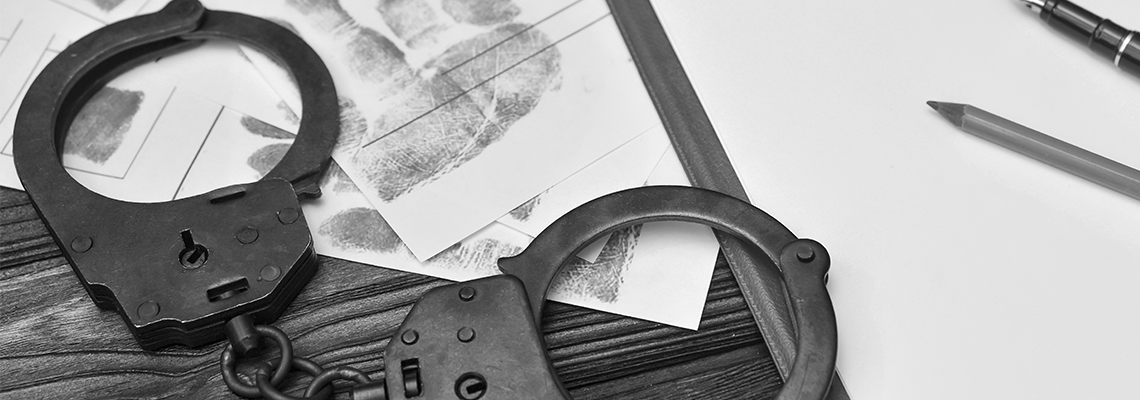 Handcuffs, fingerprints of the detained criminal, a blank sheet of paper on the background of a wooden table.