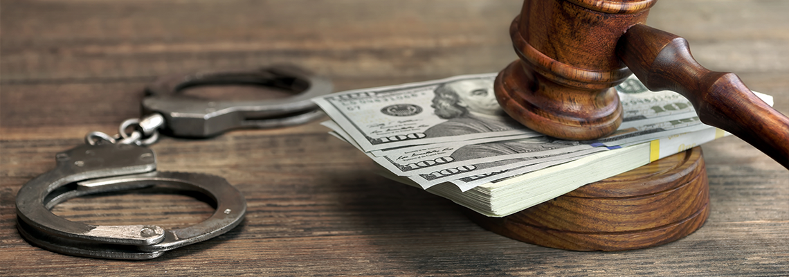 Dollar banknotes, handcuffs and judge gavel on wood table.